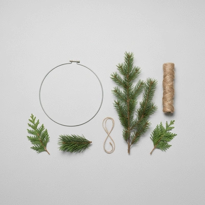 Assortment of minimalist wreath crafting materials like a metal hoop, greenery, and twine on a clean background
